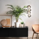 Lampa wisząca LED Bolla 17W 3000K w kolorze chromu z dymionymi kloszami, zawieszona nad ciemnym stolikiem w nowoczesnym wnętrzu. Otoczona roślinami w doniczkach, z elementami dekoracyjnymi w tle.