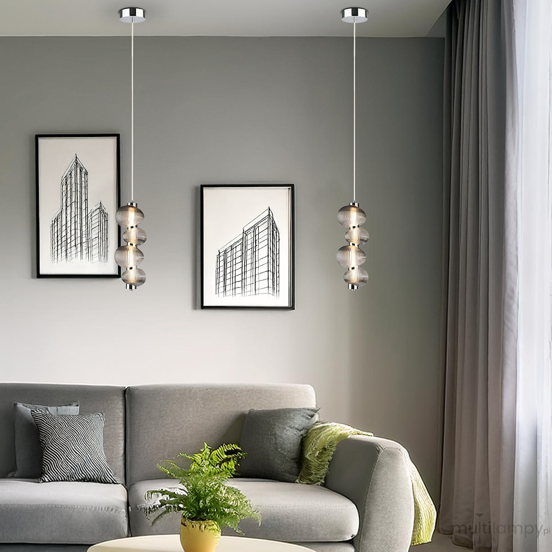 Lampa wisząca LED Bolla 17W 3000K w chromowanej oprawie z dymionymi kloszami, zawieszona na cienkim kablu. W tle widoczna szaro-beżowa ściana, kanapa z poduszkami i roślina doniczkowa.