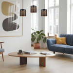 Lampa wisząca Morgan z trzema źródłami światła E27 w czarnej obudowie z ażurowym wzorem, zawieszona w salonie nad okrągłym stołem. W tle widoczne okna oraz roślina w doniczce, a także meble w stonowanych kolorach.