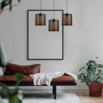 Lampa wisząca Morgan w kolorze czarnym z trzema kloszami E27, o ażurowym wzorze, zawieszona na długich kablach. W tle widoczna kanapa w odcieniu brązu oraz roślina doniczkowa.