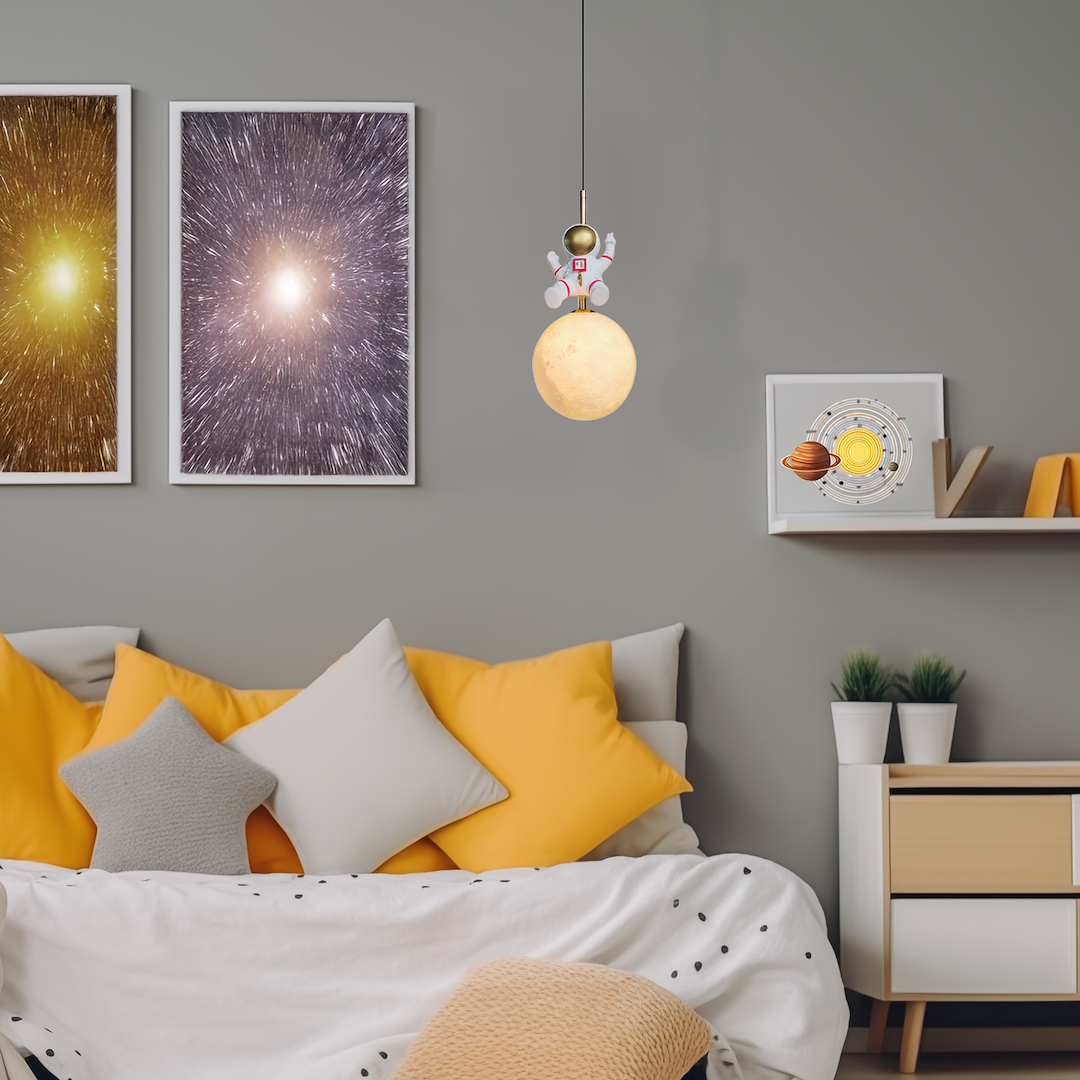 Lampa wisząca Astronauta z kloszem w kształcie księżyca w kolorze białym, zawieszona na czarnym kablu. Na górze znajduje się złoty element oraz figurka astronauty w białym skafandrze.