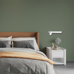 Kinkiet Magnet 1xGU10 w białym kolorze, zamontowany na zielonej ścianie obok łóżka. Oświetlenie skierowane w dół, z lampą LED 5W CCT. W tle widoczne poduszki, narzuta w odcieniach szarości oraz nocna szafka z dekoracjami.