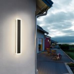 Durango 80 kinkiet elewacyjny LED 24W 4500K w kolorze czarnym, zamontowany na ścianie domu, emitujący ciepłe światło. Prosty, prostokątny kształt z podświetleniem, w tle drewniane krzesła na tarasie oraz chmurzyste niebo.