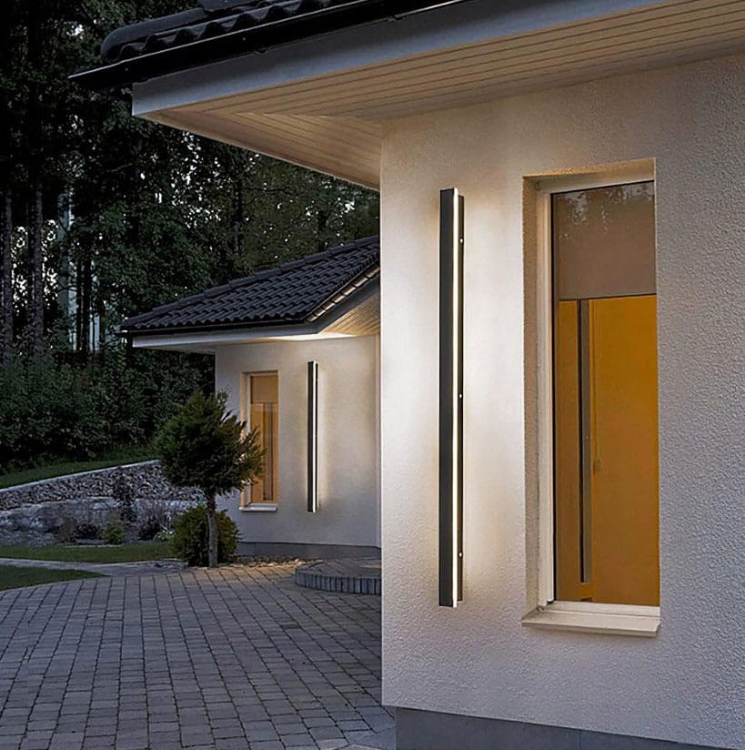 Lara 150 kinkiet elewacyjny LED 45W 4000K w kolorze czarnym, prostokątny, zamontowany na ścianie budynku. Emituje jasne światło, oświetlając elewację. Widoczny w kontekście zewnętrznym, obok okna i zieleni.
