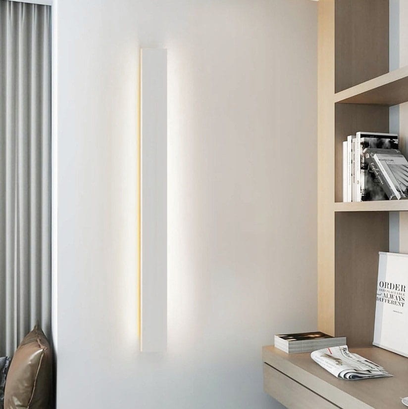Kinkiet elewacyjny LED Lara 100 w kolorze białym, o prostokątnym kształcie, zamontowany na ścianie. Emisja światła o temperaturze 4000K, w otoczeniu nowoczesnego wnętrza z regałem i dekoracjami.