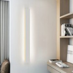 Kinkiet elewacyjny LED Lara 100 w kolorze białym, o prostokątnym kształcie, zamontowany na ścianie. Emisja światła o temperaturze 4000K, w otoczeniu nowoczesnego wnętrza z regałem i dekoracjami.