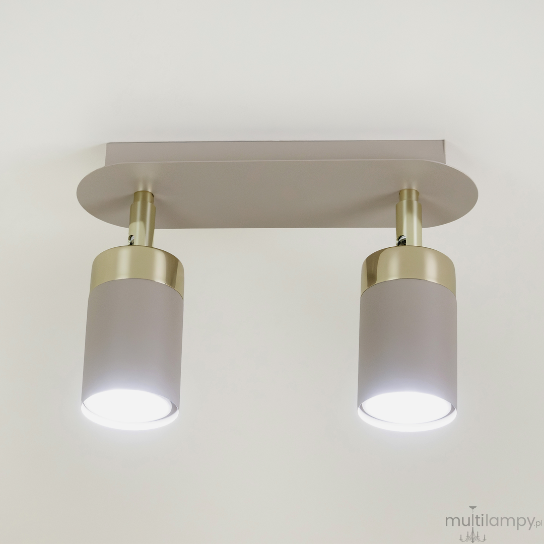 Lampa sufitowa Joker z dwoma spotami w kolorze kaszmiru i złota, montowana na prostokątnej podstawie. Lampy mają cylindryczny kształt, z jasnym światłem emitowanym przez żarówki GU10.