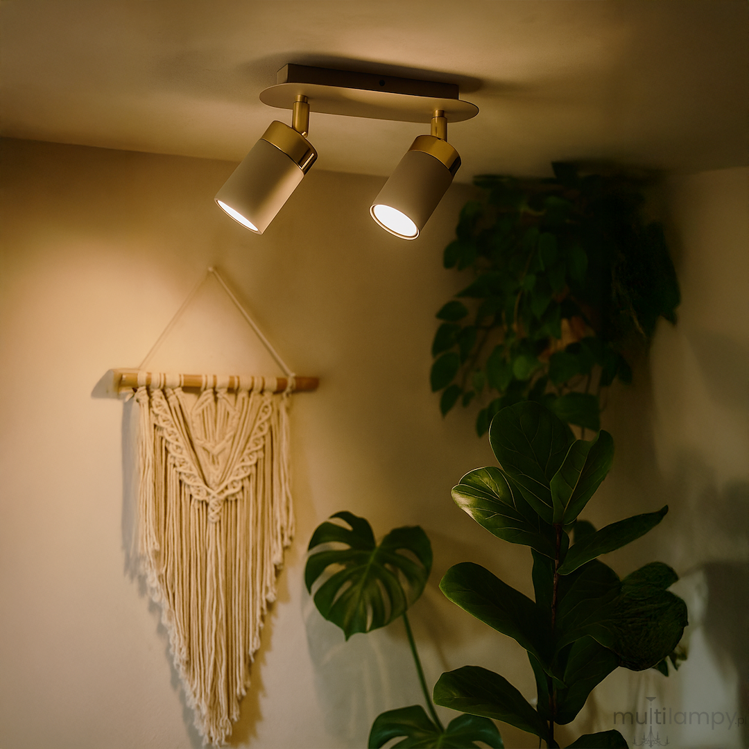Lampa sufitowa Joker w kolorze kaszmiru i złota z dwoma ruchomymi reflektorami GU10, zamontowana na suficie. W tle widoczne dekoracje ścienne oraz roślinność, co tworzy przytulną atmosferę.