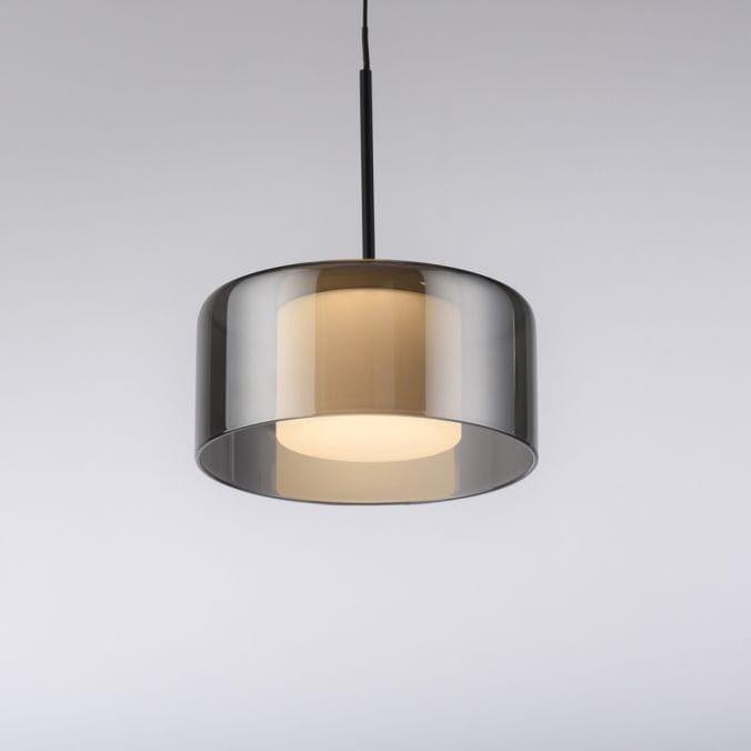 Lampa wisząca LED Rika 6W w kolorze czarnym dymionym, o okrągłym kształcie z półprzezroczystym kloszem. Zawieszona na cienkim czarnym przewodzie, z jasnym źródłem światła w środku. Tło jasne, proste.