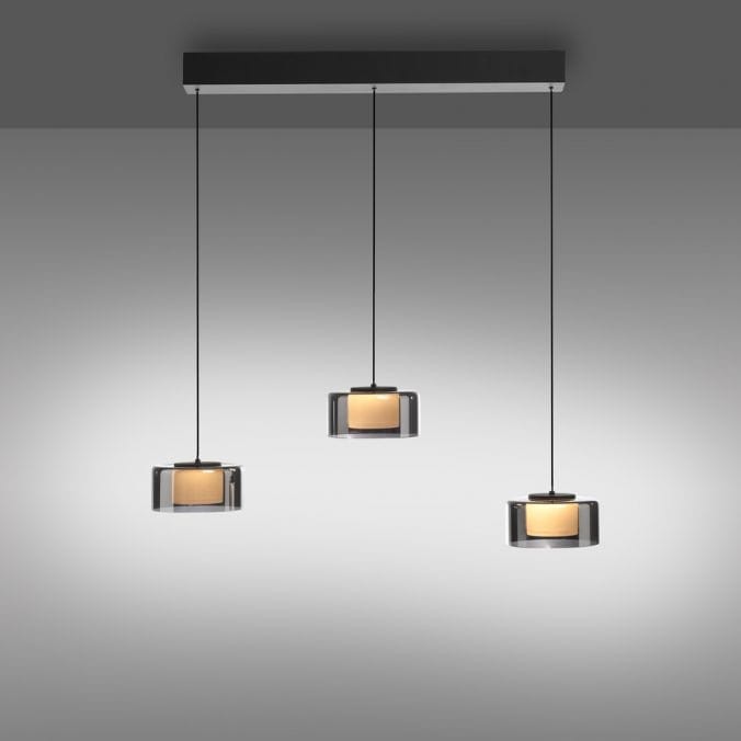 Lampa wisząca Rika z trzema kloszami LED 18W w czarnym dymionym kolorze. Klosze mają okrągły kształt, a długi kabel umożliwia regulację wysokości. Elementy metalowe w kolorze czarnym, umocowane na prostokątnej podstawie.