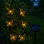 Girlanda solarna o długości 580 cm z 20 diodami LED w kształcie motylków, umieszczona na zielonym tle roślin. Motylki mają przezroczyste skrzydła z delikatnym wzorem, a obok znajduje się panel słoneczny. Całość podświetlona ciepłym światłem.