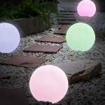 Kula D30 lampa ogrodowa LED RGB, w kształcie dużej, białej kuli, emitująca różne kolory. Ustawiona na ścieżce z kamiennych płyt, otoczona żwirem, w otoczeniu roślinności. Widoczna kula zmienia kolory na różowo, zielono i niebiesko.