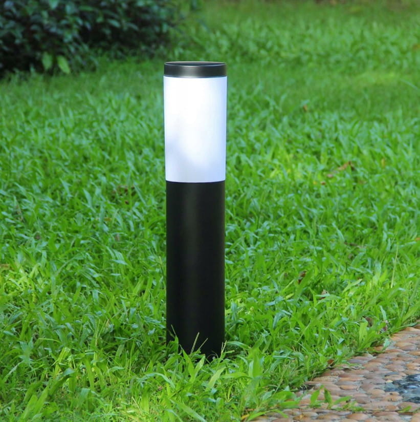 Lampa stojąca Manila H45 o okrągłej formie, z czarnym metalowym korpusem i białym kloszem, umieszczona na trawie. Produkt leży w pozycji stojącej, idealny do oświetlenia ogrodu lub ścieżek.