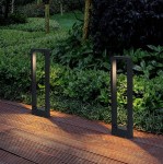 Lampa stojąca ogrodowa Rio LED H60 w kolorze antracytowym, w formie prostokątnego słupka. Ujęcie z boku, na tle zieleni. Emituje ciepłe światło, umieszczona na drewnianym podłożu, co podkreśla nowoczesny design.