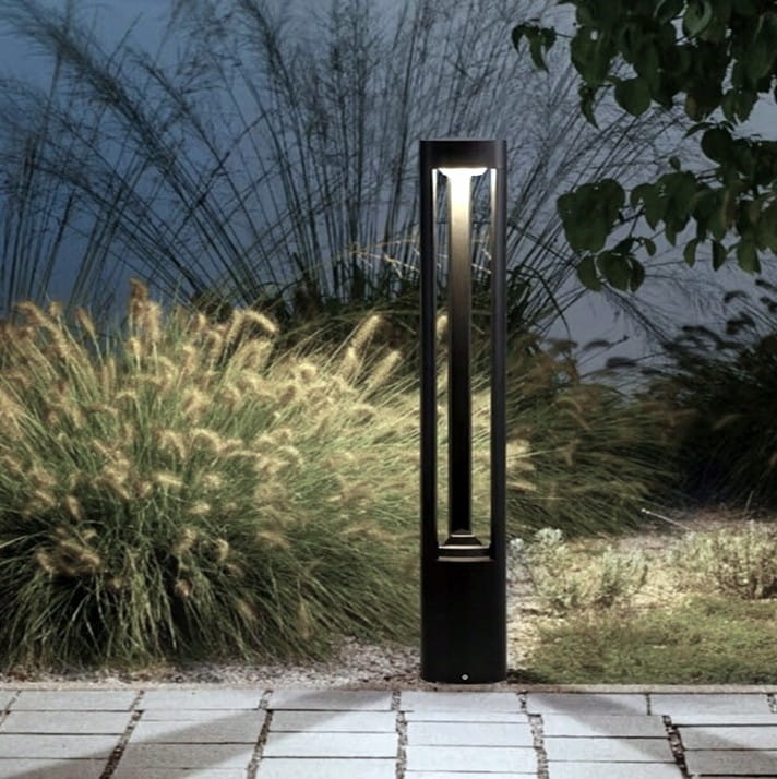 Lampa stojąca ogrodowa Mario H80 w kolorze antracytowym, o prostokątnym kształcie, z wbudowanym źródłem światła GX53. Ujęcie frontalne, umieszczona na płaskiej powierzchni, otoczona trawami ozdobnymi.