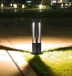 Lampa stojąca ogrodowa Mario H50 w kolorze antracytowym, z cylindrycznym korpusem oraz przezroczystymi panelami, emituje światło w otoczeniu trawnika. Ujęcie z boku, ukazujące oświetlenie oraz cień na ziemi.