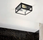 Czarna lampa sufitowa elewacyjna Lidio z dwoma żarówkami E27, o kwadratowym kształcie i metalowej konstrukcji. Ujęcie z dołu, zawieszona na suficie, z widocznymi żarówkami w środku. Tło w neutralnych odcieniach, z marmurową ścianą po prawej.