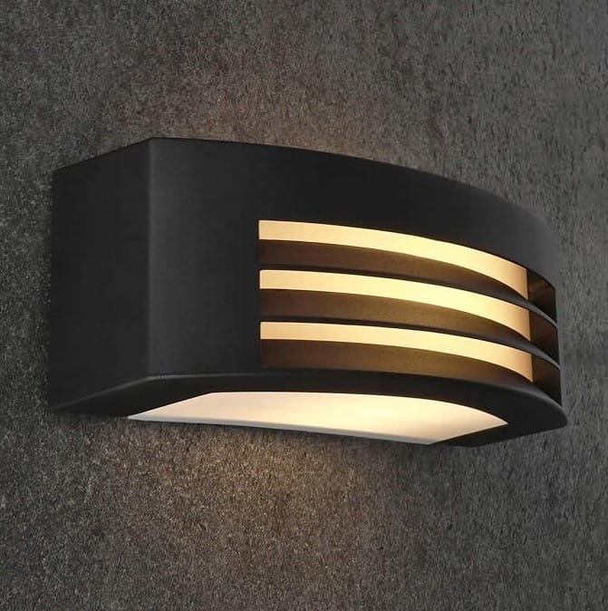 Kinkiet elewacyjny Corso w kolorze antracytowym, o nowoczesnym, zaokrąglonym kształcie, z dekoracyjnymi pionowymi szczelinami, emitującym ciepłe światło. Montowany na ścianie, idealny do oświetlenia zewnętrznego.