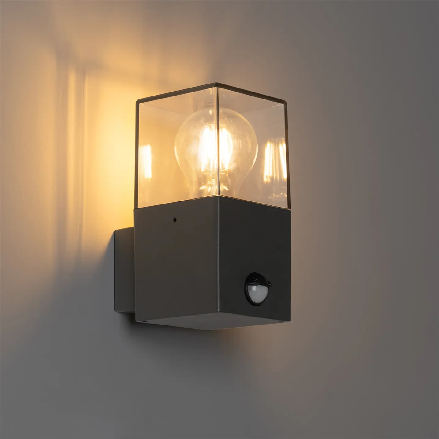 Czarny kinkiet zewnętrzny Denver z czujnikiem ruchu, z przezroczystą osłoną, zawierający żarówki E27. Ujęcie z boku, pokazujące oświetlenie oraz detale konstrukcyjne, w tym mały czujnik ruchu na dolnej części.