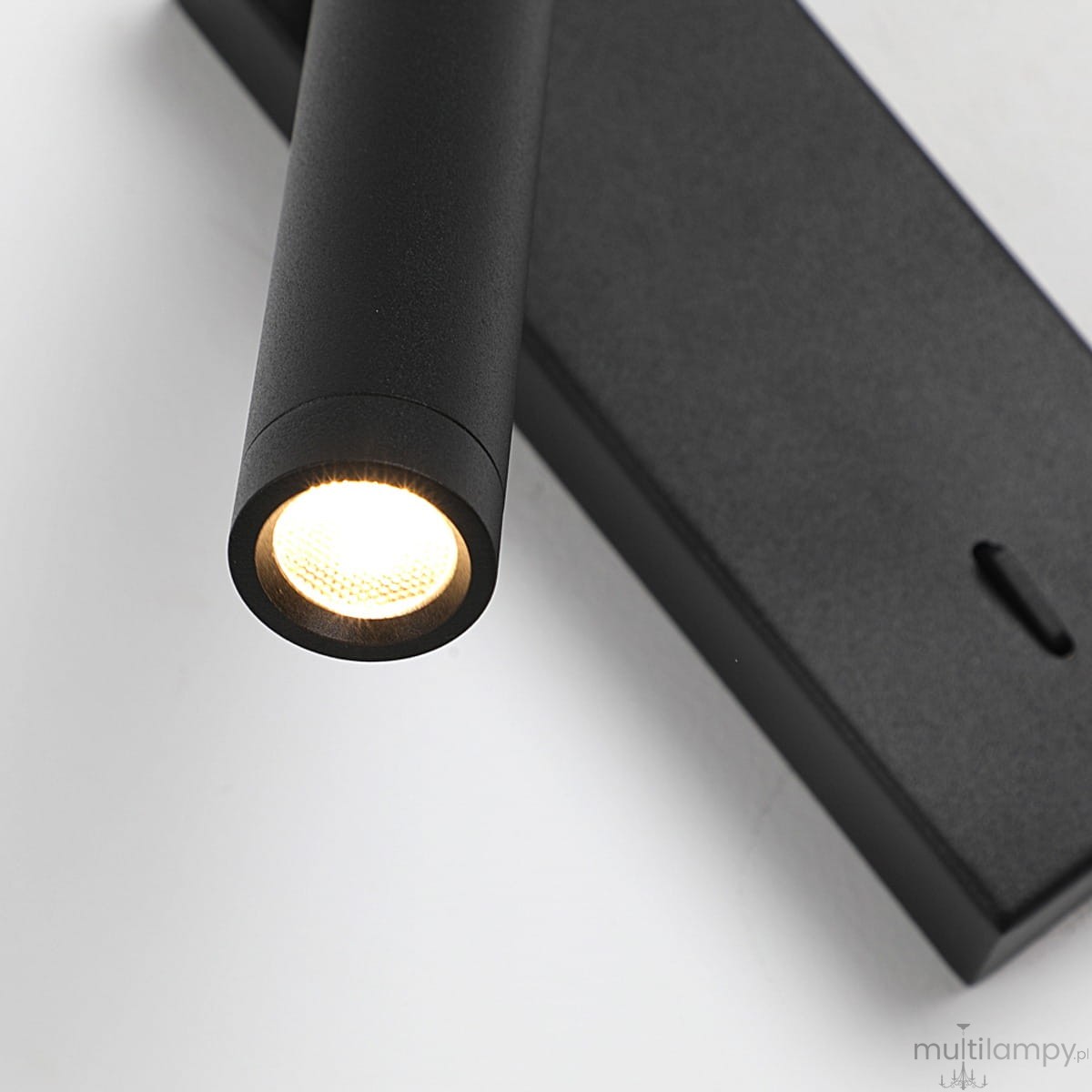 Cali kinkiet spot 1xLED 2,5W w kolorze czarnym, z cylindryczną oprawą lampy, zamocowany na prostokątnej podstawie. Źródło światła emituje ciepłe, białe światło, a powierzchnia ma matowe wykończenie. Kąt ujęcia zbliżony na detal.