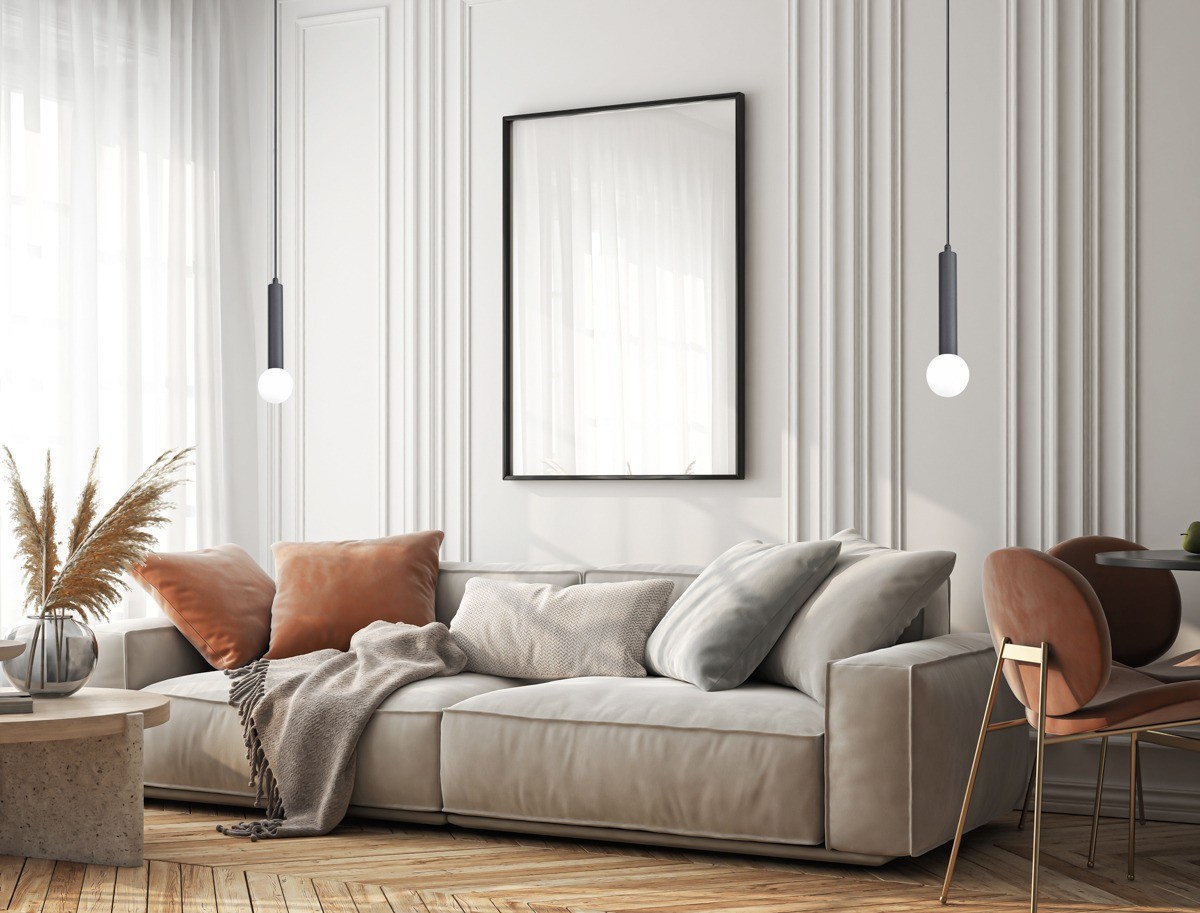 Lampa wisząca Filano 1xG9 w kolorze czarnym, zawieszona w nowoczesnym wnętrzu. Główna część lampy ma cylindryczny kształt, z białą żarówką na końcu. Otoczenie to jasny pokój z sofą, poduszkami i dekoracjami roślinnymi.