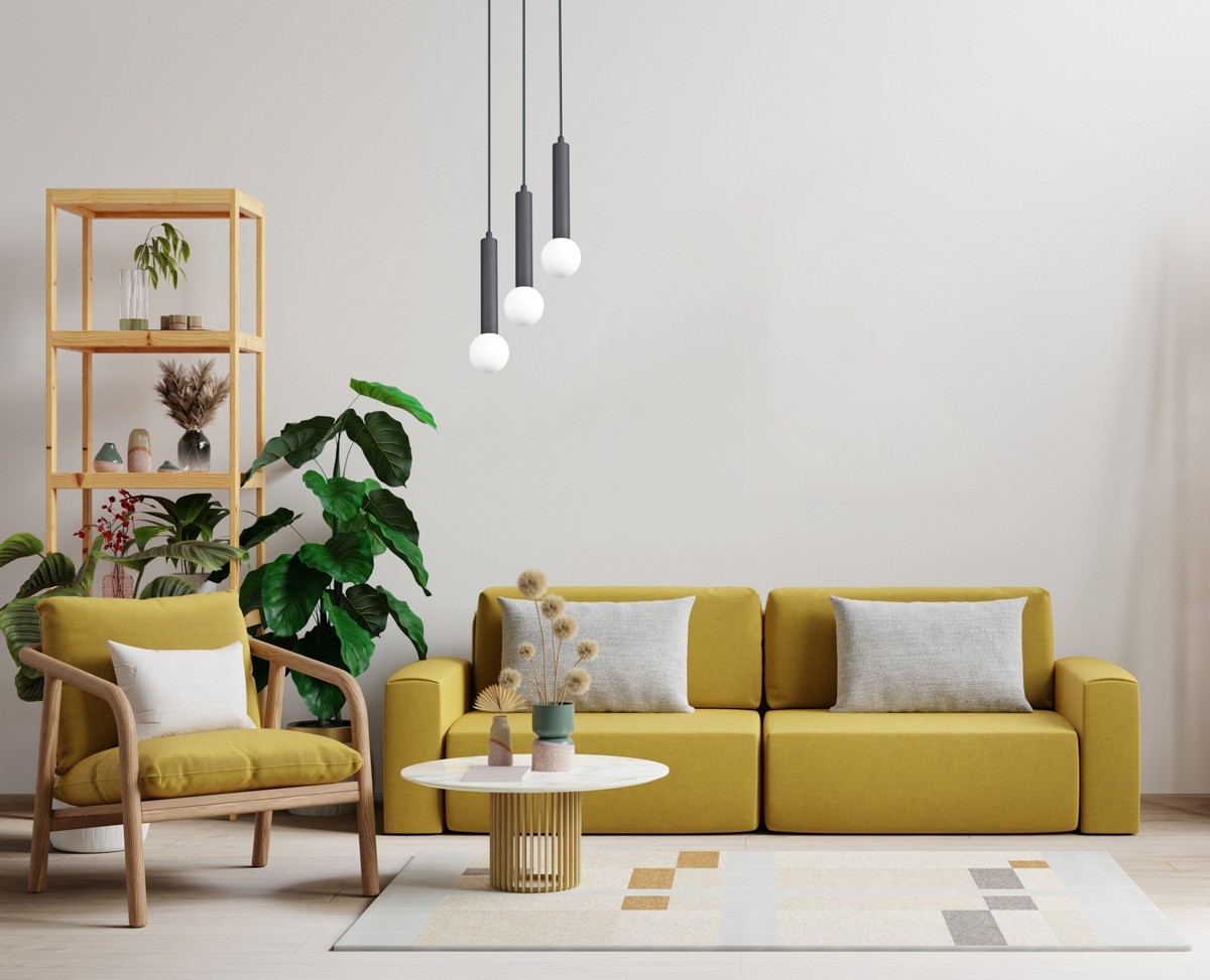 Lampa wisząca Filano 3xG9 w kolorze czarnym z trzema okrągłymi kloszami, zawieszona na długich przewodach. Ujęcie frontalne, w tle żółta sofa i drewniana półka z roślinami. Tło jasne, minimalistyczne.