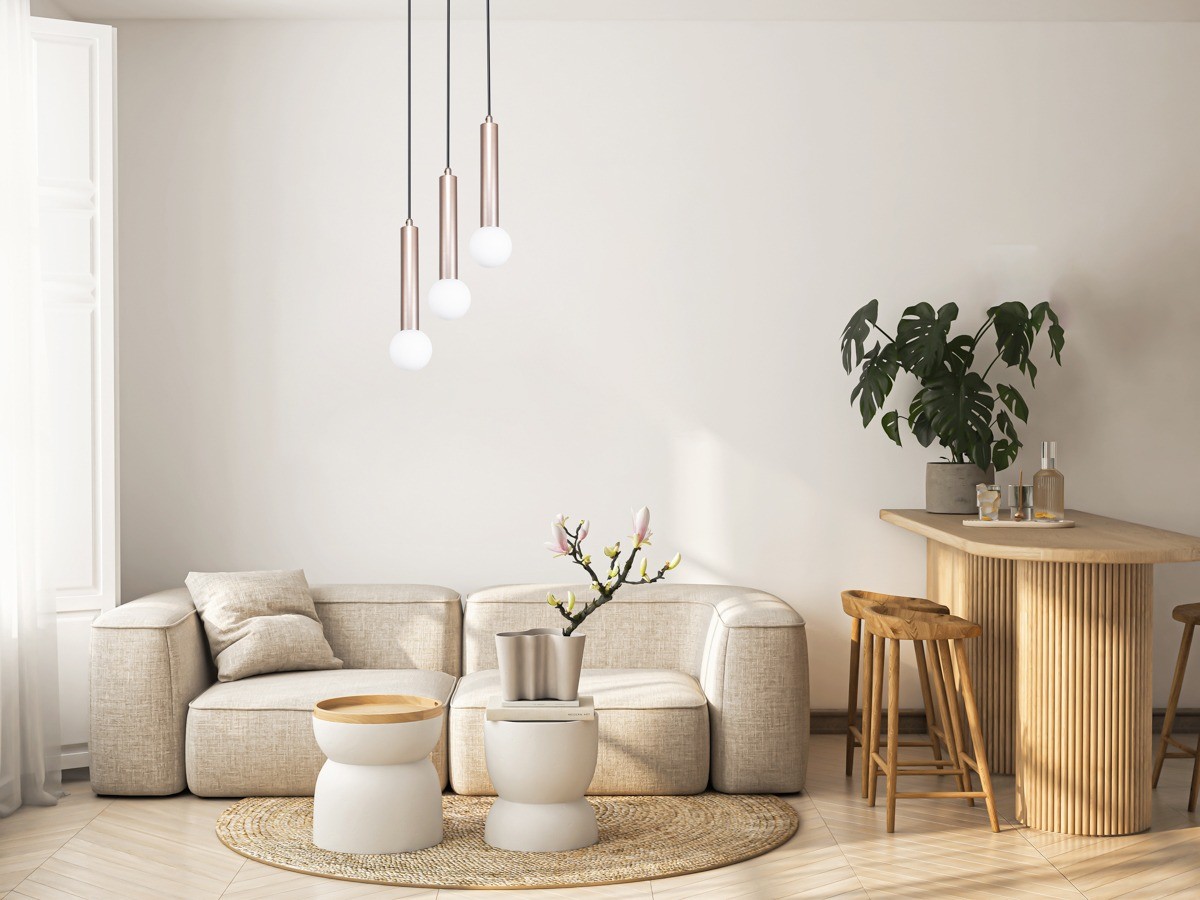 Lampa wisząca Filano 3xG9 w kolorze kawowym z trzema okrągłymi kloszami, zawieszona na czarnych przewodach. Produkt umieszczony w nowoczesnym wnętrzu z jasnym narożnikiem, drewnianym stołem oraz rośliną na tle stonowanej ściany.