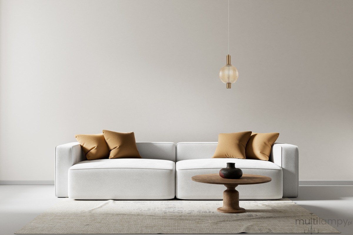 Lampa wisząca Lenti 1xLED 7W w kolorze złotym z bursztynowym kloszem, zawieszona nad białą kanapą z brązowymi poduszkami. Okrągły, przezroczysty klosz z żłobieniami, montowana na długim przewodzie. Minimalistyczne otoczenie z drewnianym stolikiem.