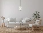 Lampa wisząca Nico 2xLED 8W w kolorze złotym i białym, o zaokrąglonym kształcie, zawieszona na długim przewodzie. W tle widoczny jasny salon z białą sofą, okrągłym dywanem i roślinnością.
