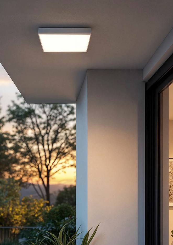 Biały panel natynkowy LED Mora 24W CCT IP44, kwadratowy, zamontowany na suficie. Oświetlenie emituje ciepłe światło, w tle widoczna zieleń i zachód słońca, co podkreśla jego zastosowanie na zewnątrz.