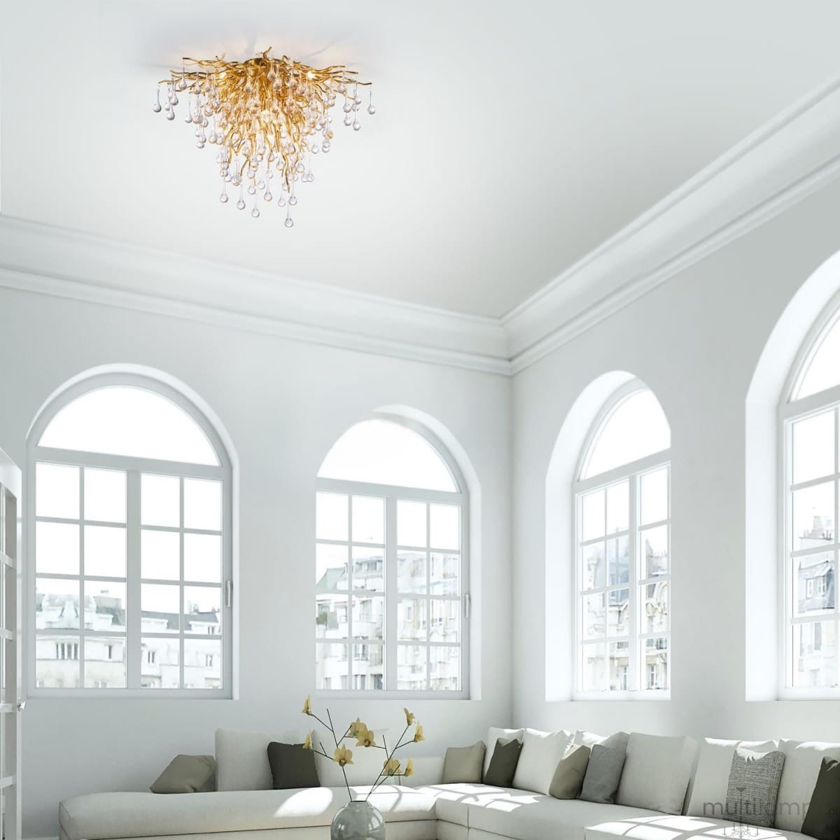 Lampa sufitowa Icicle w postarzanym mosiądzu z dziewięcioma gniazdami G9, o organicznej formie przypominającej gałęzie, z dekoracyjnymi kryształowymi kroplami, montowana na suficie w jasnym wnętrzu z dużymi oknami.