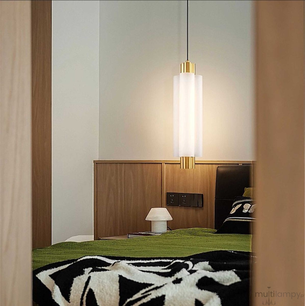 Lampa wisząca LED Osmo 9W 3000K w kolorze mosiądzu, cylindryczna, z matowym kloszem. Zawieszona na cienkim przewodzie, oświetla nowoczesne wnętrze sypialni, w tle zielony koc i nocna lampka.