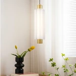 Lampa wisząca LED Osmo 9W 3000K z mosiężnymi detalami i matowym kloszem, zawieszona na czarnym przewodzie. W tle widoczne rośliny doniczkowe oraz jasne zasłony.