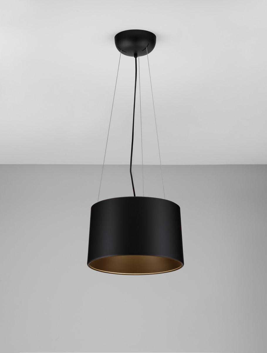 Lampa wisząca Bajo z jedną żarówką LED 24W, o cylindrycznym kształcie, w matowym czarnym kolorze z wewnętrzną złotą powłoką. Zawieszona na cienkim przewodzie, w aranżacji na jasnym tle.