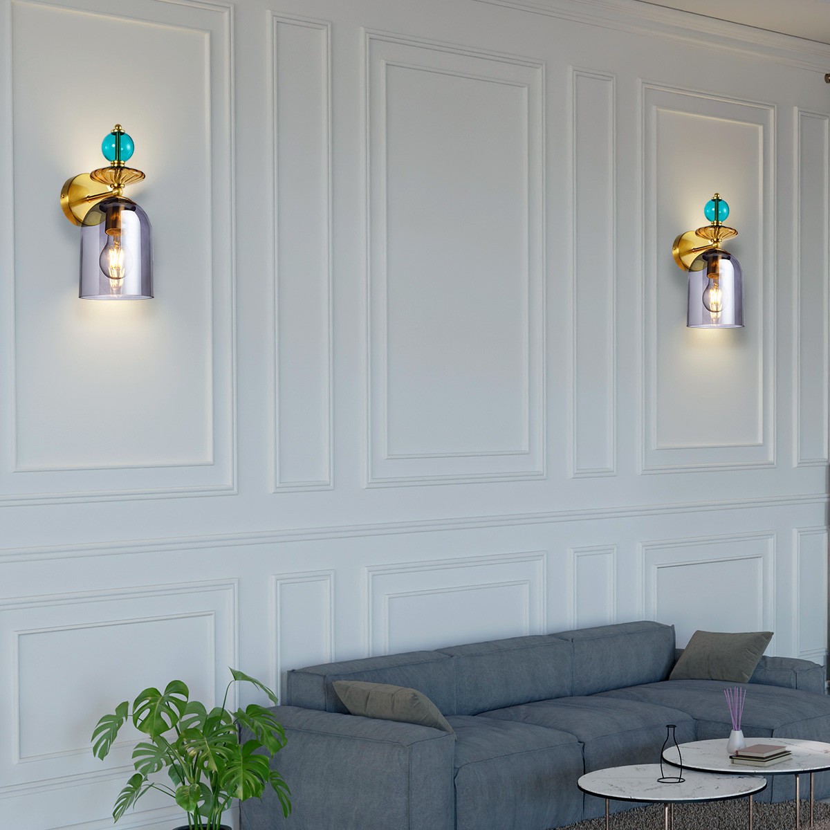 Kinkiet Tropea 1xE27 w kolorze złotym z dymionym kloszem. Ozdobny element z niebieską dekoracją, montowany na ścianie. Widoczny na tle jasnej, eleganckiej ściany. Produkt o nowoczesnym designie, idealny do aranżacji wnętrz.