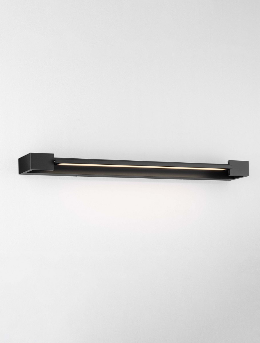 Kinkiet Justo 1xLED 17W w kolorze czarnym, prostokątny, zamontowany na ścianie. Posiada minimalistyczny design z delikatnym podświetleniem LED. Tło jasne, co podkreśla elegancki wygląd lampy.