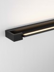 Kinkiet Justo 1xLED 17W w kolorze czarnym, zamontowany na ścianie. Prosty, prostokątny kształt z wąskim źródłem światła LED, emitującym ciepłe światło. Tło jasne, co podkreśla minimalistyczny design lampy.