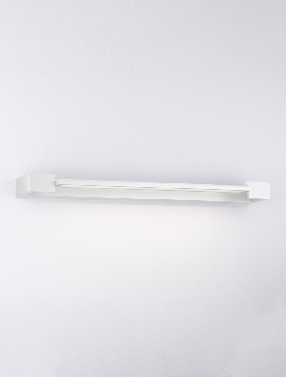 Justo kinkiet 1xLED 17W w kolorze białym, prostokątny, zamontowany na ścianie. Oświetlenie LED umieszczone w długiej, cienkiej obudowie, emitujące jasne światło. Tło jednolite, jasne, co podkreśla design lampy.