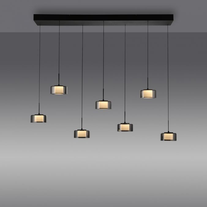 Lampa wisząca Rika z siedmioma źródłami światła LED 56W w czarnym, dymionym kolorze. Posiada prostokątne klosze zawieszone na cienkich linkach, umieszczone na prostokątnej podstawie. Ujęcie frontalne, na jednolitym tle.