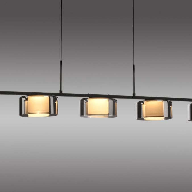 Lampa wisząca Rika z pięcioma źródłami LED, o mocy 42W, w kolorze czarnym dymionym. Produkt zawiera przezroczyste klosze w kształcie cylindrów, zawieszone na cienkich linkach w poziomej konfiguracji.