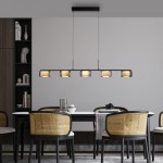 Lampa wisząca Rika z pięcioma źródłami LED, czarna z dymionym kloszem, zawieszona nad stołem. Klosze mają lekko złotawy odcień, a lampa zwisa z prostokątnej podstawy. Otoczenie to nowoczesna jadalnia z krzesłami ratanowymi.
