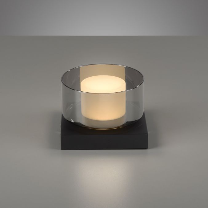 Lampa sufitowa LED Rika 4,5W w czarnym dymionym kloszu, z okrągłym białym źródłem światła umieszczonym na prostokątnej podstawie. Produkt ustawiony na szarym tle, w pozycji stojącej.