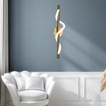 Kinkiet LED Meleca 12W CCT w kolorze złotym, z eleganckim, spiralnym kształtem i białym akcentem świetlnym. Zamontowany na ścianie, w tle widoczna jasna kanapa w stylu skandynawskim. Idealny do nowoczesnych wnętrz.