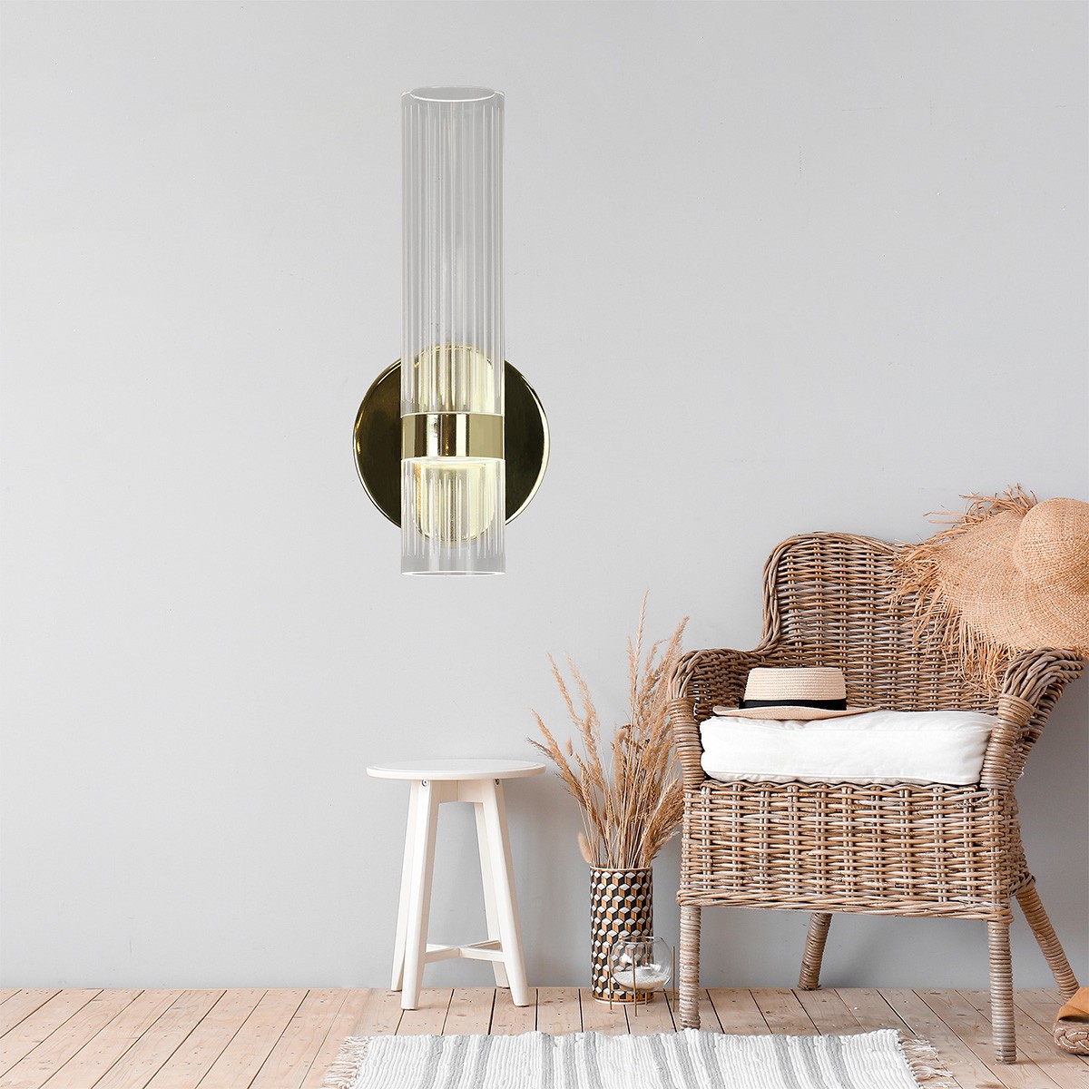 Kinkiet LED Ambiente 18W CCT w kolorze złotym, z przezroczystym kloszem o pionowych żłobieniach, montowany na okrągłej podstawie. Produkt zamontowany na szarej ścianie, w otoczeniu mebli i dekoracji.