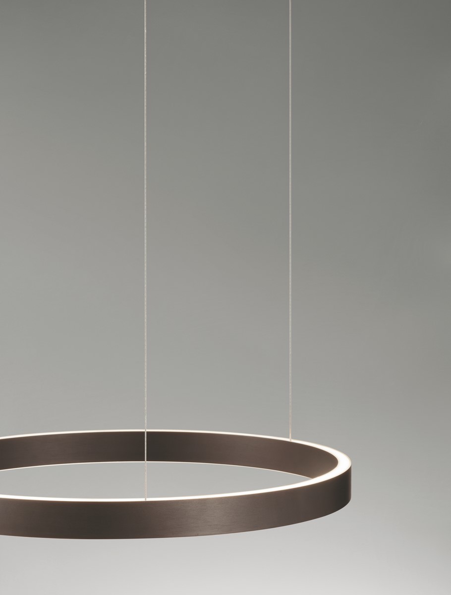 Brązowa lampa wisząca Bari D60 z jedno źródło LED 60W, o okrągłym, matowym kształcie. Zawieszona na cienkich linkach, emituje delikatne światło z krawędzi, idealna do nowoczesnych wnętrz. Tło w jasnym odcieniu podkreśla jej elegancki design.