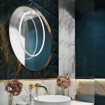 Kinkiet LED Mirror D60 o okrągłym lustrze, z białym podświetleniem, umieszczony na ciemnoniebieskiej ścianie z dekoracyjnymi płytkami. Złota ramka oraz rośliny dekoracyjne w tle, z umieszczonym na blacie umywalki.