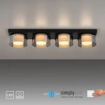 Lampa sufitowa Rika z czterema źródłami światła LED 26W, w czarnym dymionym kolorze. Ułożona na płaskiej podstawie, z przezroczystymi kloszami, emitującymi ciepłe światło. Widoczna technologia ściemniania.