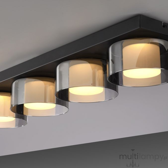 Czarna lampa sufitowa Rika z czterema źródłami światła LED, każdy z przezroczystym, dymionym kloszem. Produkt zamontowany na prostokątnej podstawie, z delikatnym, ciepłym światłem. Idealna do nowoczesnych wnętrz.