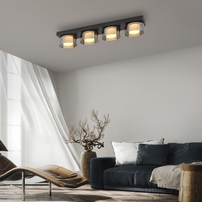 Lampa sufitowa Rika 4xLED 26W w czarnym dymionym wykończeniu. Produkt umieszczony na suficie, z czterema okrągłymi kloszami, emitującymi ciepłe światło. Otoczenie obejmuje jasny salon z dużym oknem i ciemnoszarym sofą.