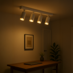 Lampa sufitowa Mica z czterema reflektorami GU10 w białej obudowie z chromowanymi detalami. Zawieszona na prostokątnej listwie, emitująca ciepłe światło. Widoczna w nowoczesnym wnętrzu z drewnianym biurkiem, rośliną i obrazem na ścianie.